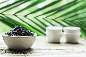 Spa - composition with stones, beauty jars and Black Sea salt on a wooden table. Green leaves in the background, blur.