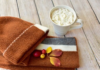 Cozy warm wooden toque and scarf with colourful fall leaves arranged in decorative autumnal background to represent autumn 
