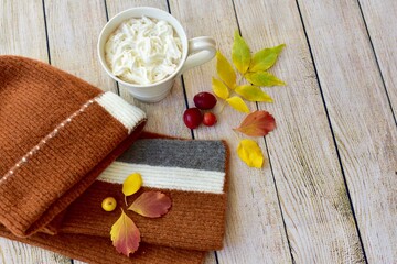 Cozy warm wooden toque and scarf with colourful fall leaves arranged in decorative autumnal background to represent autumn 