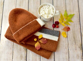 Cozy warm wooden toque and scarf with colourful fall leaves arranged in decorative autumnal background to represent autumn 