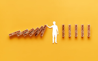 pre-corona and post-corona. human figure stops falling wooden blocks labeled pre-corona and builds...