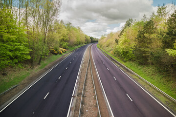 A quiet dual carriage motorway devoid of traffic with trees on either side and a blue sky above