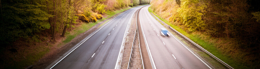 Speeding blurred car on a dual motorway with autumn trees in background - dangerous speed.