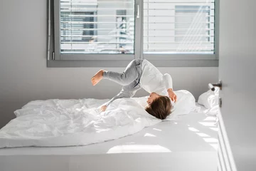 Foto op Plexiglas Happy little child boy jumping on bed doing somersault having fun at home at sunny morning. © Tetiana Soares