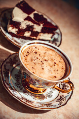 A piece of chocolate cake on a plate, coffee in the background