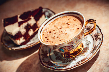 A piece of chocolate cake on a plate, coffee in the background