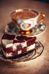 A piece of chocolate cake on a plate, frothy coffee in a golden cup in the background