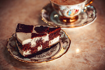A piece of chocolate cake on a plate, frothy coffee in a golden cup in the background