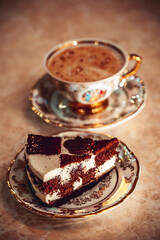 A piece of chocolate cake on a plate, frothy coffee in a golden cup in the background