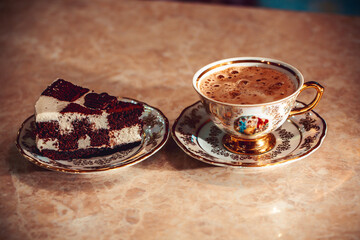 A piece of chocolate cake on a plate, frothy coffee in a golden cup in the background