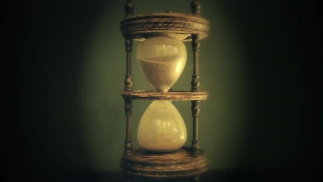 Fine sand falling from the top half of a magnificent hourglass (an ancient device for the measurement of time). Backlit timelapse, green and yellow color tones.
