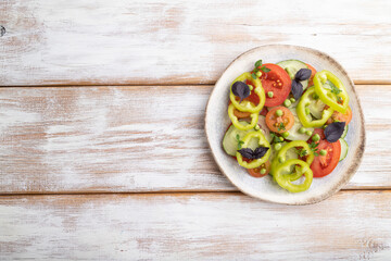 Vegetarian salad from green pea, tomatoes, pepper and basil on white wooden background. top view, copy space.
