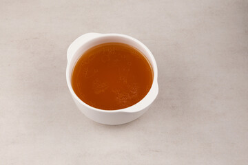 Beef bone broth  in white bowl on a stone surface. Healthy beverage with natural collagen. Selective focus, copy space