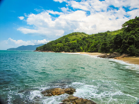 Clear and calm waters gently lapping against rocks at Praia do Cedro in Ubatuba, with untouched, deserted beach and preserved nature on a sunny day