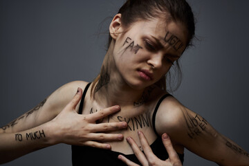offended woman with angry inscriptions on her body touches herself with her hands on a gray background aggression 