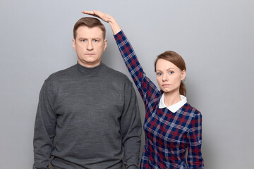 Short woman is standing on tiptoes and showing height of tall man