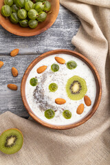 Yogurt with kiwi, gooseberry, chia and almonds in wooden bowl on gray wooden background. top view, flat lay.