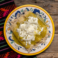 Mexican green enchiladas with chicken and cheese on wooden background