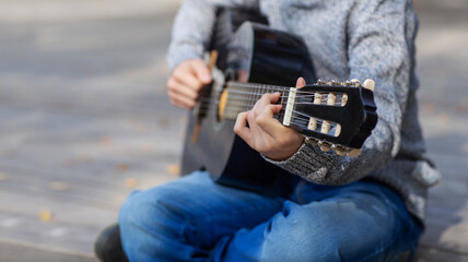 teen boy plays black acoustic guitar on an autumn day in the Park
