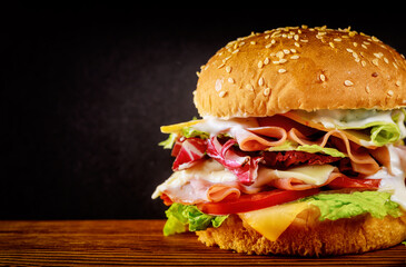 Burger with lettuce, cheese, ham and tomato on dark background.