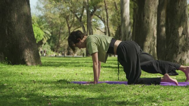 Profile shot of a fit woman doing a yoga sequence on an urban park. High quality 4k footage