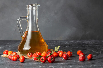 Glass bottle of hawthorn vinegar with Fresh ripe red/yellow hawthorn fruits on rustic background. Crataegus monogyna berries