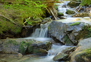 Original nature photograph of a small waterfall cascading over rocks with green foliage