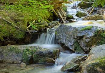 Fototapeta premium Original nature photograph of a small waterfall cascading over rocks with green foliage