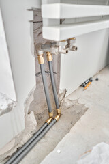 connection heating pipes to white Radiator in a new apartment under construction. Work As A Plumber, mounting water heating radiator on the white wall indoors