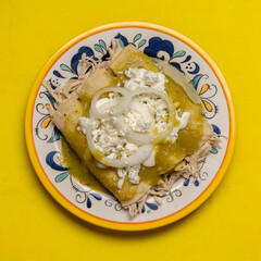 Mexican green enchiladas with chicken and cheese on yellow background