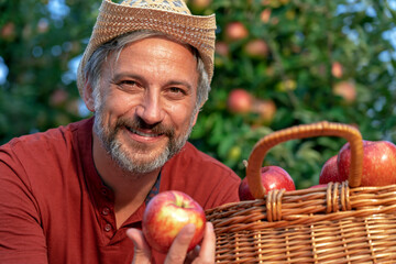 Charismatic Handsome Farmer with Hat Holding Red Apple in Sunny Orchard