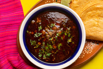Mexican birria consome soup and tacos on yellow background