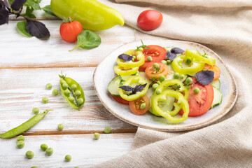 Vegetarian salad from green pea, tomatoes, pepper and basil on white wooden background. Side view.