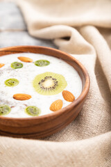 Yogurt with kiwi, gooseberry, chia and almonds in wooden bowl on gray wooden background. Side view, close up, selective focus.