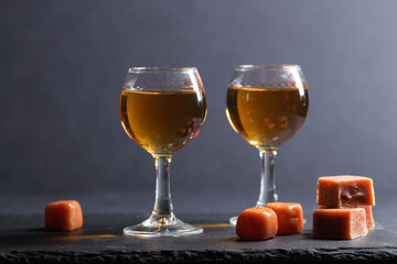 Glass of whiskey with caramel candies on a black stone slate board on black background. Side view.