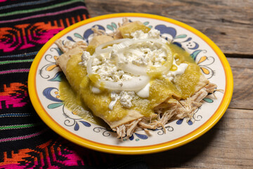 Mexican green enchiladas with chicken and cheese on wooden background