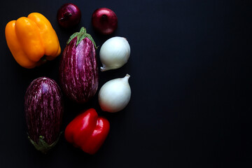 Harvest concept. Raw vegetables: eggplants, sweet pepers and onions on a dark background. Selective focus, close-up, top view. Copy space. Food background