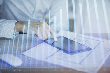 Double exposure of man's hands holding and using a digital device and forex graph drawing. Financial market concept.