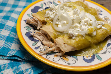 Mexican green enchiladas with chicken and cheese on wooden background