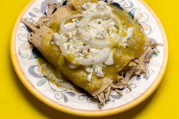 Mexican green enchiladas with chicken and cheese on yellow background