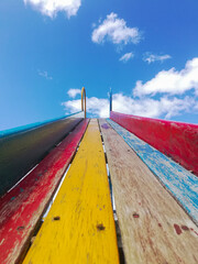 Photograph of a slide seen from below towards the sky with clouds and with old wood in a straight and colored way