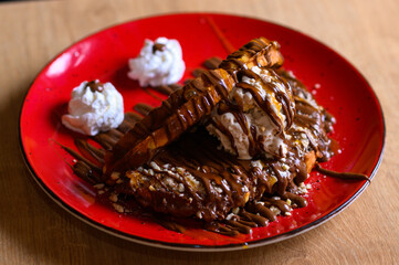 beautifully decorated caloric waffle with lots of chocolate and cream on a red plate. Smile waffle.