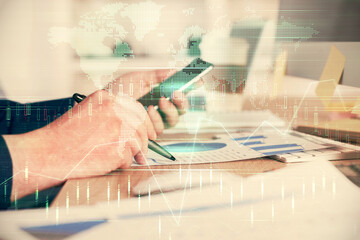 Double exposure of man's hands holding and using a phone and financial graph drawing. Analysis concept.