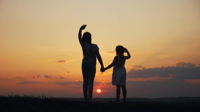 happy family two sisters sunset walks at in the park silhouette say goodbye waving hand. two daughters. kid dream concept. happy sunset family walk together. children kid walking in travel the park