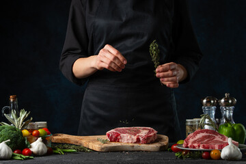 Food's photo of preparing testy steak with rosemary and other spices on wooden board on dark blue background. Traditional recipe of cooking meat. European cuisine.