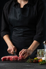 Close-up view of chef cutting with knife meat beef for preparing steak on dark background. Vertical format. Food concept.
