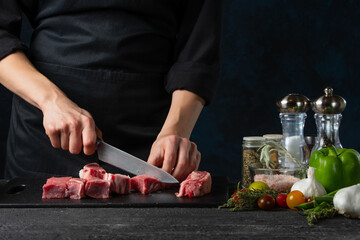 Chef cutting pork meat with knife on professional kitchen on dark blue background. Restaurant or hotel menu. Traditional recipe. Food concept.