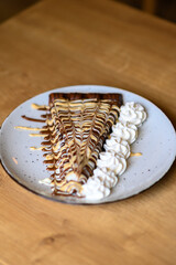 a beautifully decorated caloric pancake full of chocolate.
pancake on a red plate with lots of whipped cream.
