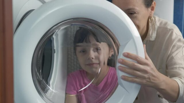 Mother with child by washing machine. A happy mother with her little daughter look through the door in the washing machine.