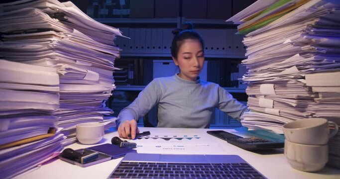 Asian business woman sitting at desk covered with stack of paperwork and talking phone, using laptop. Tired alone girl sleeping while working hard at late night. Time lapse, Fast speed, Web cam view